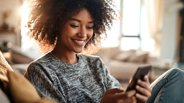 Happy African person smiling while using a digital wallet app on a smartphone or tablet in a bright modern apartment, reviewing positive financial updates such as tax refunds, credit score improvement