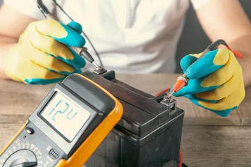 Electrician measures voltage with a multimeter, motorcycle battery close-up of hands. © Artvibe