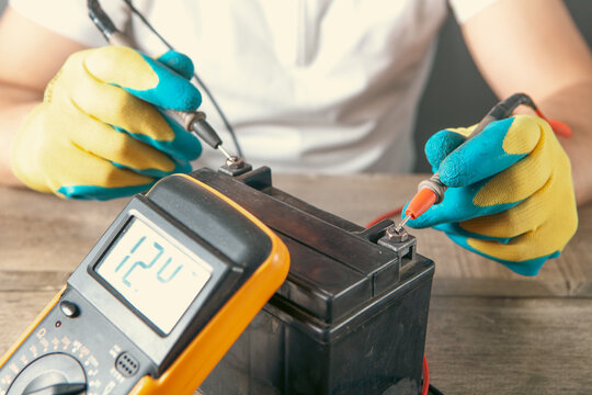 Electrician measures voltage with a multimeter, motorcycle battery close-up of hands.