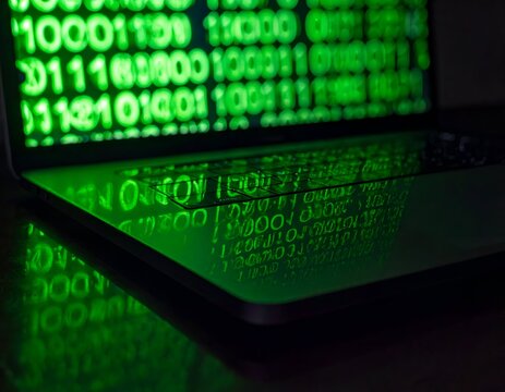 Cascading lines of green binary digital code glowing brightly on a dark computer monitor screen matrix backdrop