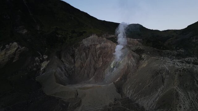 4k Drone video footage of the active crater of Mount Papandayan featuring rugged cliffs and sulfur-rich steam rising from volcanic vents in West Java, Indonesia.