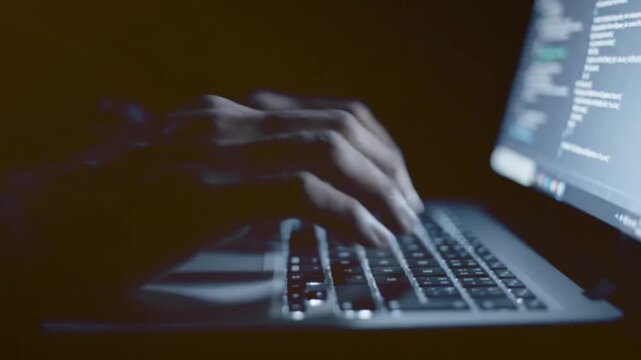 Person working on computer laptop by typing code during night hours at dark home office desk closeup shot showing focused programmer writing software scripts fast.