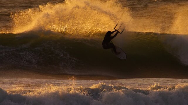 Kitesurfer carving ocean wave with glowing flying sea spray at sunset, slowmo