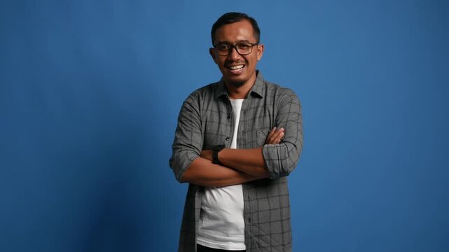 Smiling happy satisfied asian adult man look camera hold hands crossed folded isolated on blue background studio portrait. People lifestyle concept
