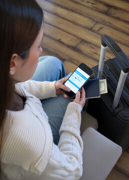 Mujer realizando check-in online desde su tel&eacute;fono m&oacute;vil junto a su equipaje, pasaporte y dinero de viaje 