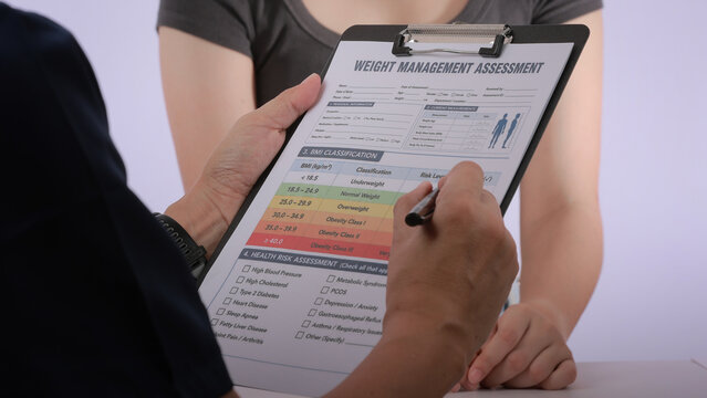 Focused dietitian holds checklist clipboard conducting weight management assessment during serious consultation with female patient seeking healthy lifestyle change