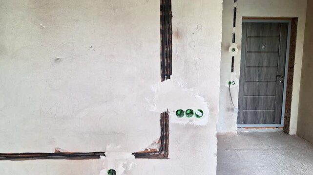 Exterior wall of a residential building featuring exposed electrical conduit, PVC plumbing pipe, and unfinished doorway. Static architectural detail showing utility infrastructure and construction