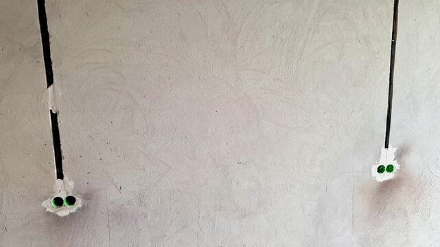 Electrical wiring and power outlets installed on a freshly plastered interior wall during home renovation. Construction progress showing unfinished electrical installation before painting