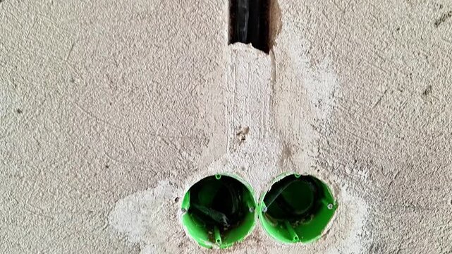 Double electrical outlet boxes installed in a freshly plastered interior wall during home renovation. Unfinished electrical installation prepared for wiring, finishing, painting, and final outlet inst