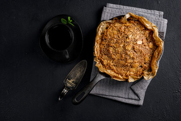 Freshly baked almond cake in a cast iron skillet served with a cup of black coffee and vintage cake server on a dark textured background © Taborisova