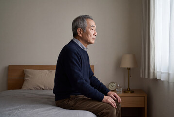 Fototapeta premium 寝室で一人静かに考え込むシニア男性。アジア人、日本人