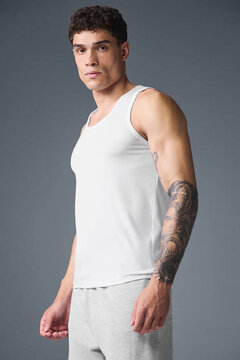 Athletic young man wearing a light gray sleeveless tank top and jogger pants, fitness apparel mockup, muscular male model with tattoo, casual activewear fashion, studio portrait, modern sportswear, bl