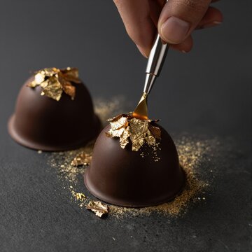 Chef decorating chocolate truffle with edible gold leaf
