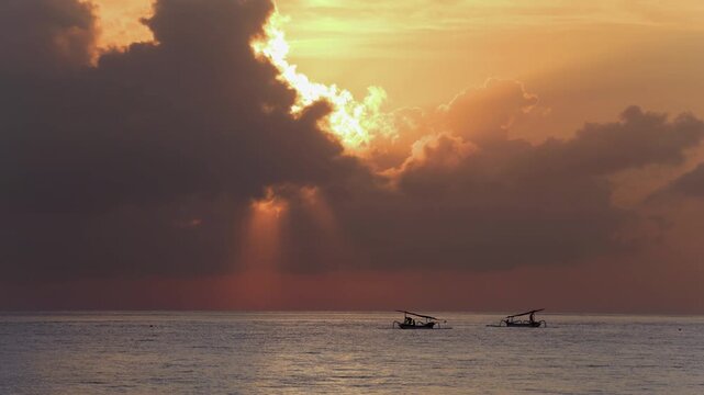 Sunrise at Nusa Penida, Bali in Indonesia. The ocean is calm, and has fishermen, fishing in jukung boats. The sky is dramatic and epic with warm, red hues. 