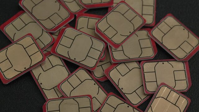 A collection of SIM cards with distinctive red borders scattered across a textured dark surface. Useful for technology marketing or telecommunications features.