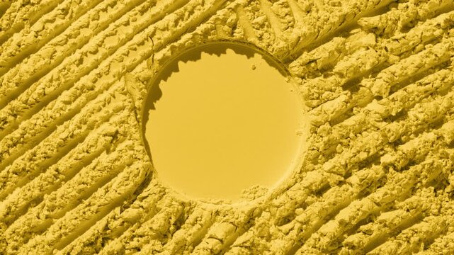 Overhead perspective shot of yellow natural powder surface with intersected furrows and round imprint in the middle illuminated with orbiting directional light producing dynamic shadows