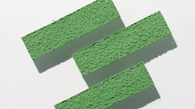 View from above shot of green powder sifted through three stripe shaped stencil on transparent surface casting moving shadow on a subtle grey surface underneath