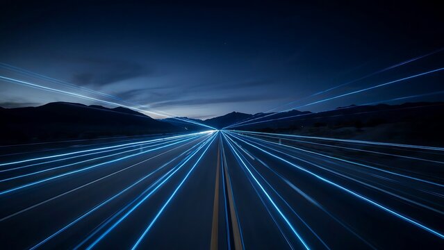 A dark road stretches into the distance with vibrant blue light trails on a nighttime highway surrounded by mountains.