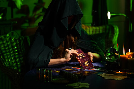 Fortune teller reading tarot cards at table in dark room