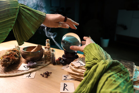 Fortune tellers hands with crystal ball reading future at table in room, closeup