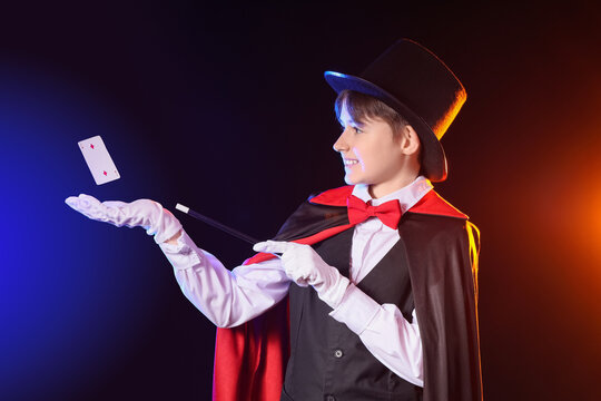 Little magician with wand and levitating playing card on dark background