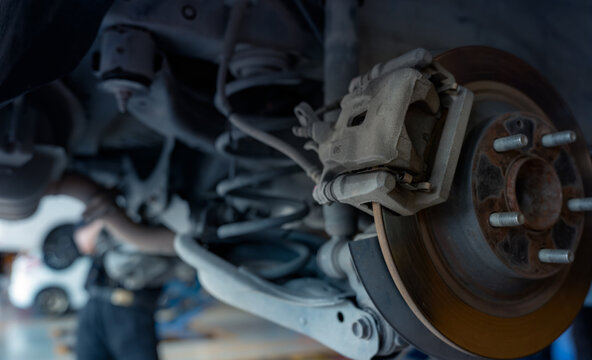 Car disc brake system. Car suspension in process of new tire replacement at garage workshop. Car disc brake mechanic check and repair. Disk break rotor. Car in change tire process at service station.