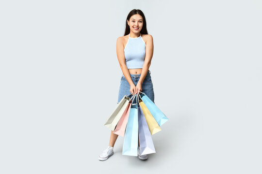 Fashionable young Asian woman in stylish denim skirt with shopping bags on grey background