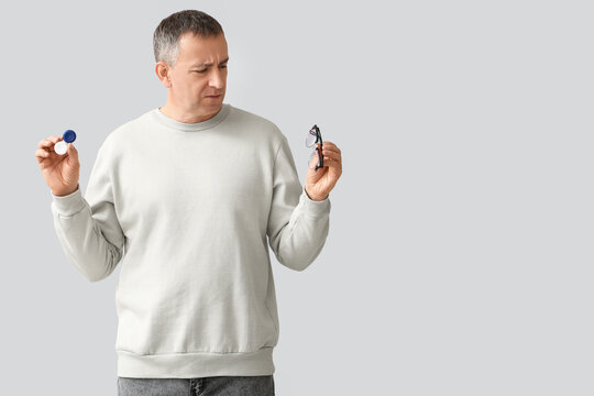 Mature man with contact lens case and eyeglasses on grey background