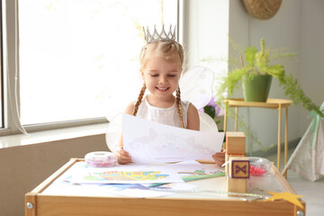 Obraz premium Cute little girl dressed as fairy with drawing at home