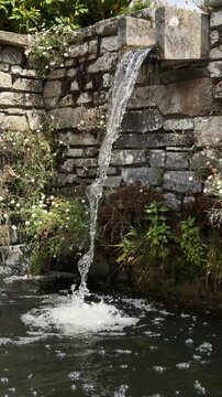 Relaxing view of fresh water pouring down from a rustic stone wall waterfall feature.
