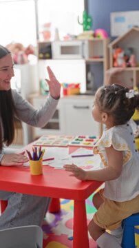 Woman gives high five with hand to little girl over drawings on red table in building; play learning bonding joy.