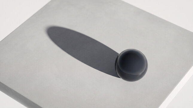 Sph&egrave;re noire minimaliste projetant une longue ombre sur un socle blanc
