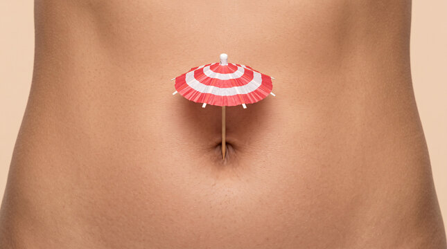 Petit parasol de plage plac&eacute; dans le nombril d&rsquo;un ventre f&eacute;minin