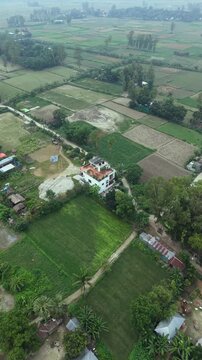 Aerial drone view of lush green agricultural fields and a modern white house surrounded by trees