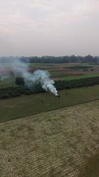Aerial drone view of agricultural field with smoke rising from small fire and people tending to