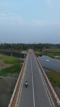 Aerial drone view of a long bridge over a river with vehicles and a motorcycle traveling across a