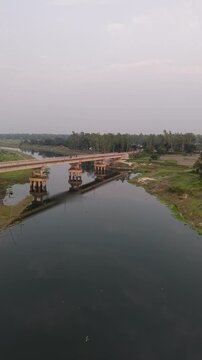 Aerial drone view of a long concrete bridge spanning a calm river reflecting the sky and