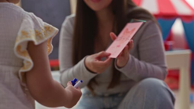 Woman holding flashcards labeled lemon and showing them to a little girl while seated on the floor in a building play area; nurturing learning.