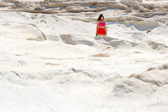   
A woman walks among the bright white volcanic rock formations of Sarakiniko on Milos Island, Greece, under strong summer sunlight, capturing the island&rsquo;s unique lunar landscape and adventure spirit