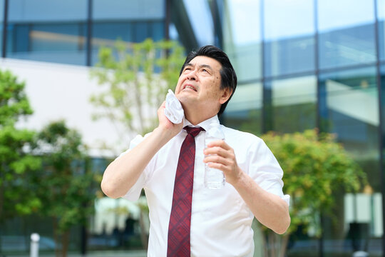 暑い屋外で汗を拭くビジネスマン