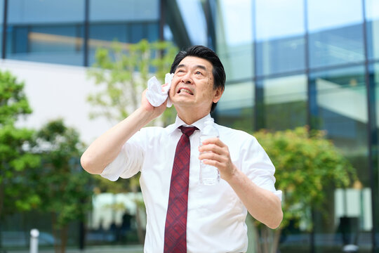 暑い屋外で汗を拭くビジネスマン