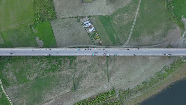 Aerial drone view of a long straight highway bridge crossing agricultural fields with vehicles