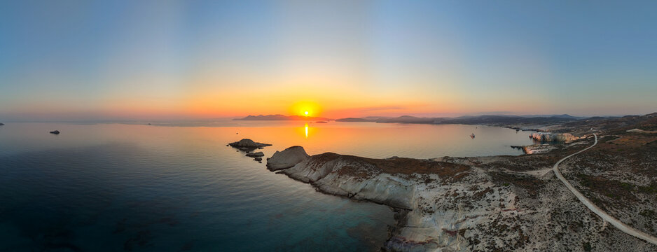 Golden sunrise over the rocky Sarakiniko coastline on Milos Island, Greece, with calm Aegean waters, soft reflections, and serene morning light across the Cyclades landscape.