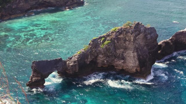 Natural rock arch near Diamond Beach, Bali, Indonesia. Dramatic cliffs and crystal-clear turquoise waters of the Bali Sea.