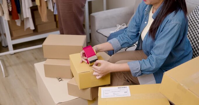 Asian woman small business owner closes parcel box after packing order, managing e-commerce shipment process, supporting home based online selling workflow during daily work