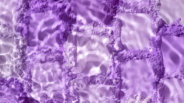 Top view extreme close-up slow motion shot of a water stream splashing over countless violet colored smears of powder arranged in a mosaic pattern