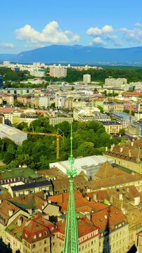 Vertical video. Geneva, Switzerland. St. Pierre Cathedral, its slender green copper spire and mismatched towers rising above the terracotta rooftops of the Old Town, Drone footage under a bright summ