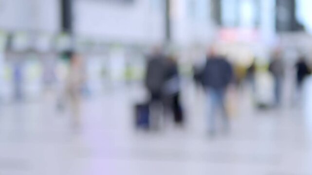 Blurred travelers move through bright, modern transit hall. People carry luggage, walk casually, and appear focused on journeys. Scene suggests airport or train station ambiance