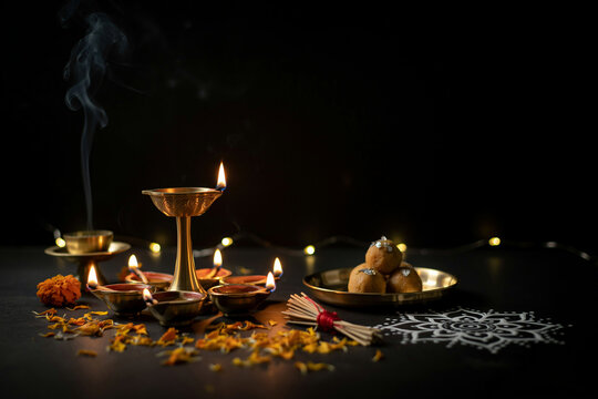 Traditional Diwali diya lamps with burning oil wicks, golden brass oil lamp and sweet laddu on dark background, spiritual Hindu festival celebration