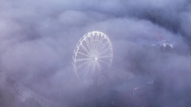 Ferris wheel emerging through fog in Palanga, Lithuania at sunset, dreamy scenic view.